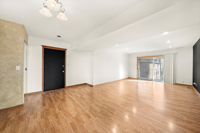 empty room with a notable chandelier, light wood-type flooring, and baseboards