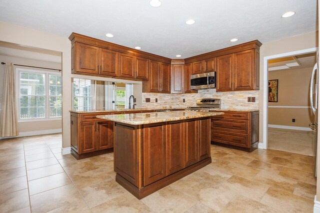 1208 Broad Creek Rd, Bloomington, IL 61704 - kitchen featuring appliances with stainless steel finishes, baseboards, backsplash, light stone countertops, and a kitchen island