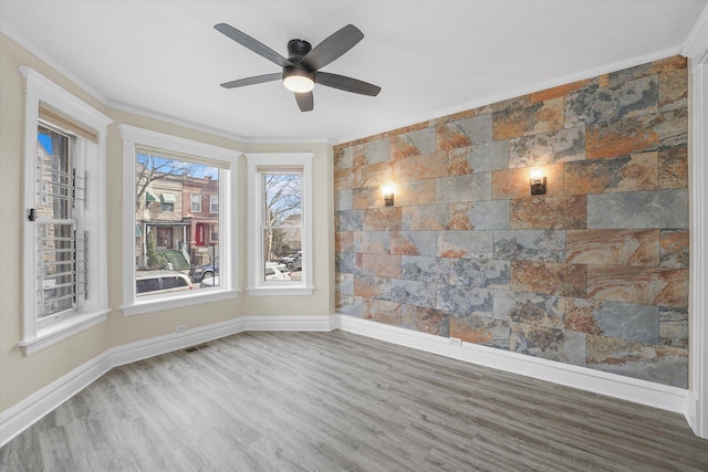 spare room featuring wood finished floors, crown molding, baseboards, ceiling fan, and an accent wall