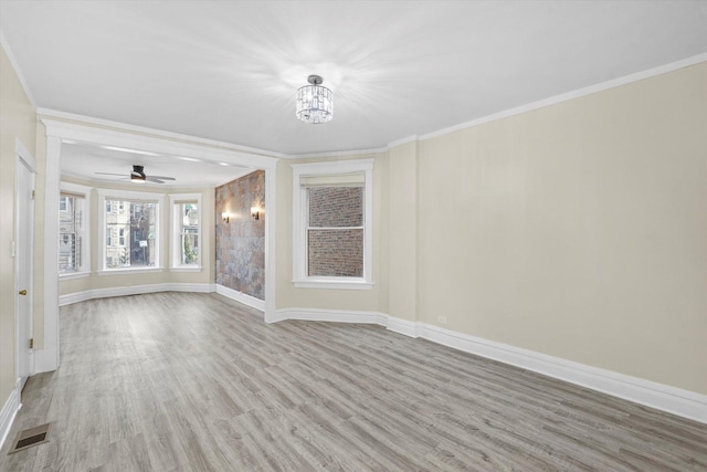 empty room with visible vents, wood finished floors, baseboards, and ornamental molding