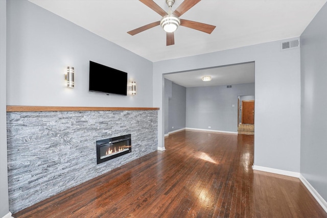 unfurnished living room featuring baseboards, visible vents, wood-type flooring, and a stone fireplace