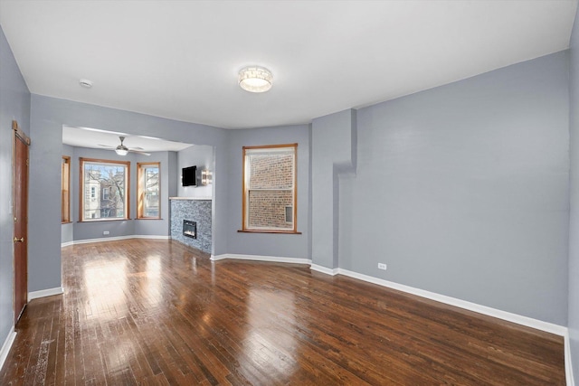 unfurnished living room with a stone fireplace, hardwood / wood-style flooring, baseboards, and ceiling fan