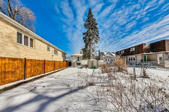 snowy yard featuring an outbuilding, a residential view, a storage unit, and a fenced backyard