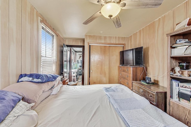 bedroom with a closet, ceiling fan, and wood walls