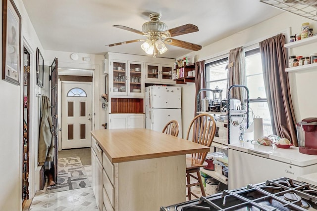 kitchen featuring a breakfast bar area, open shelves, freestanding refrigerator, glass insert cabinets, and butcher block counters