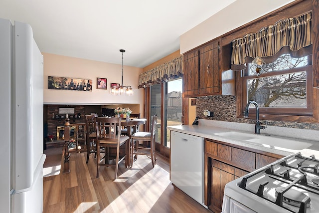 kitchen featuring a sink, wood finished floors, white appliances, light countertops, and decorative backsplash