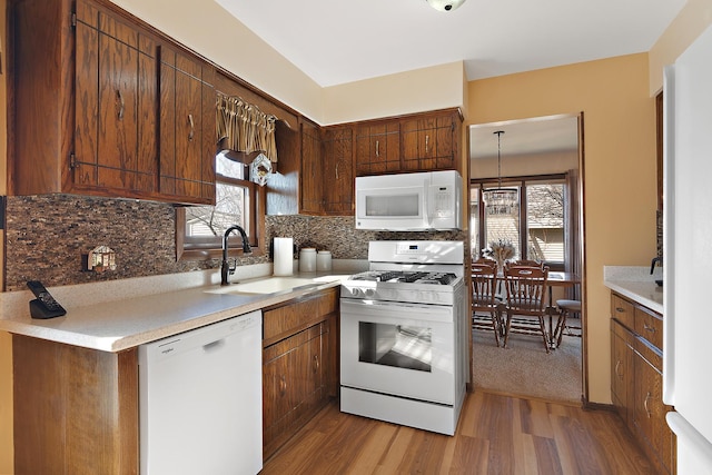 kitchen with white appliances, wood finished floors, a sink, decorative backsplash, and light countertops