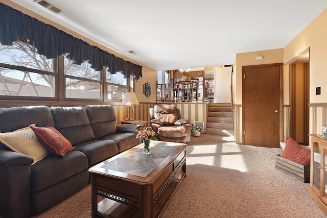 carpeted living area with visible vents, stairs, and a wainscoted wall