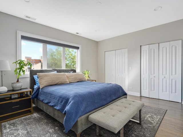 bedroom with wood finished floors, visible vents, two closets, and baseboards