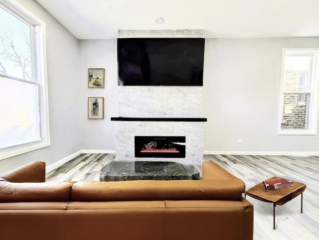 living room with baseboards, a warm lit fireplace, and wood finished floors