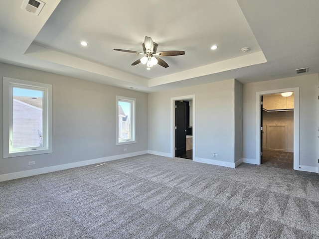 unfurnished bedroom featuring a walk in closet, a tray ceiling, baseboards, and visible vents