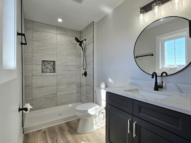 bathroom with toilet, wood finished floors, vanity, and a tile shower