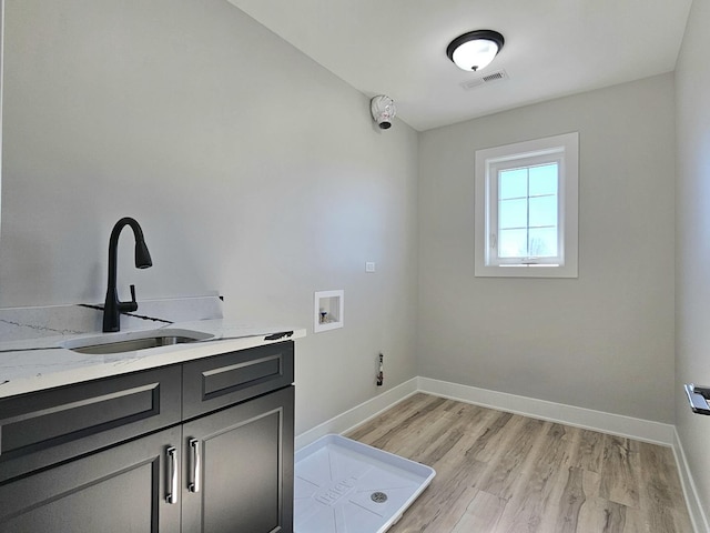 washroom with visible vents, light wood-type flooring, a sink, baseboards, and hookup for a washing machine