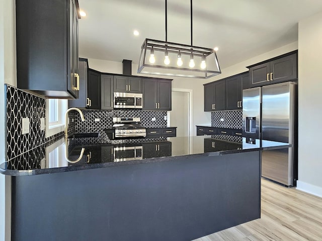 kitchen featuring decorative light fixtures, dark stone countertops, a peninsula, and stainless steel appliances