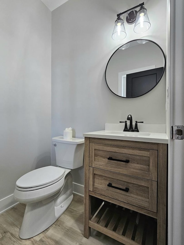 bathroom with vanity, toilet, wood finished floors, and baseboards