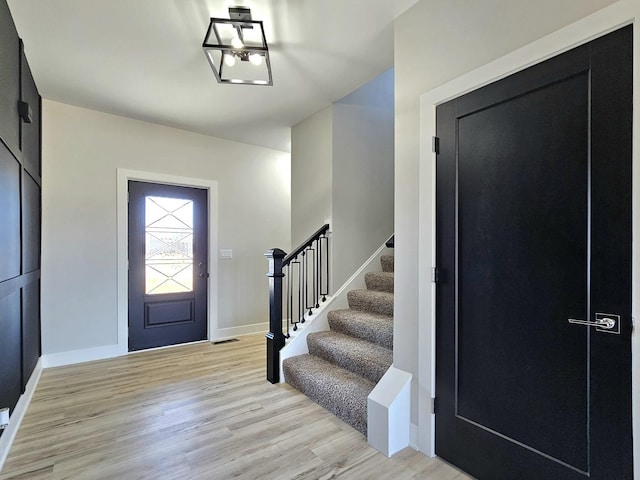 foyer entrance featuring light wood finished floors, stairway, visible vents, and baseboards