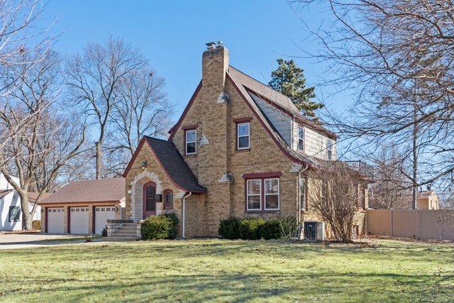 tudor-style house featuring an attached garage, a chimney, a front yard, and fence