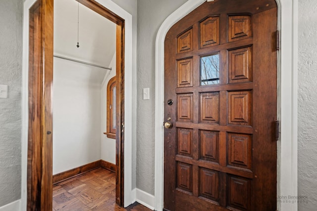 entrance foyer featuring baseboards, arched walkways, and a textured wall