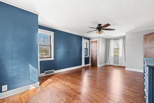 unfurnished living room with a ceiling fan, wood finished floors, visible vents, baseboards, and crown molding