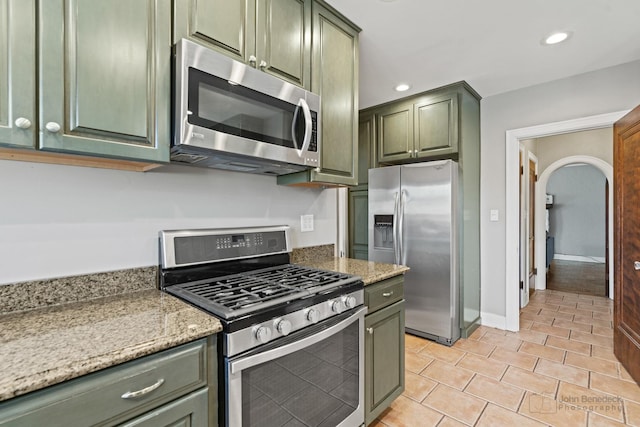 kitchen with light stone counters, recessed lighting, appliances with stainless steel finishes, arched walkways, and green cabinetry