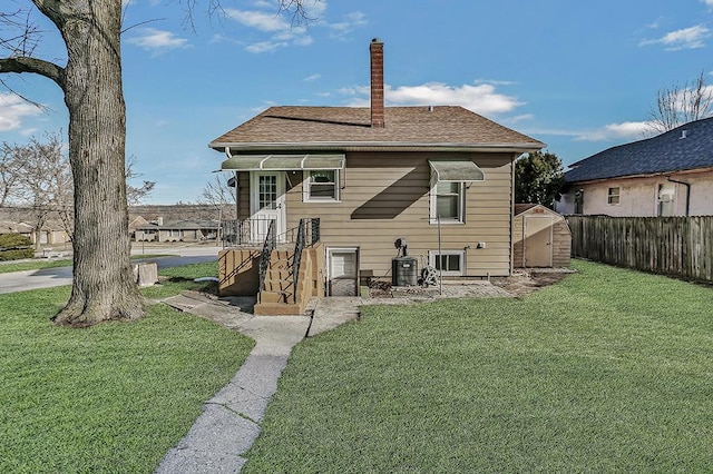 back of house featuring fence, a shingled roof, a chimney, an outdoor structure, and a lawn