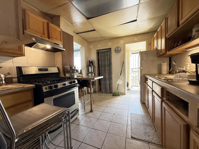 kitchen featuring a healthy amount of sunlight, stainless steel range with gas stovetop, a sink, under cabinet range hood, and brown cabinets