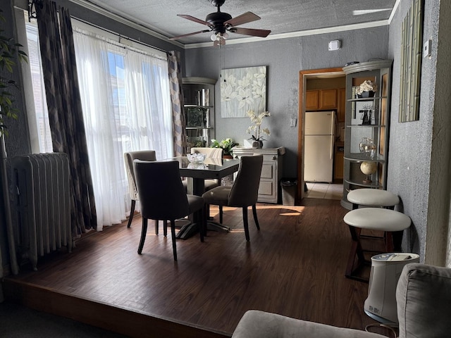 dining room with radiator heating unit, wood finished floors, a textured wall, and ornamental molding