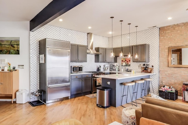 kitchen featuring wall chimney range hood, light countertops, beam ceiling, premium appliances, and light wood-style floors