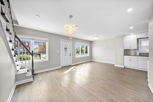 foyer featuring stairway, an inviting chandelier, light wood-type flooring, and baseboards