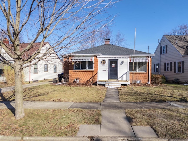 bungalow-style home featuring brick siding, a chimney, a front lawn, and a shingled roof