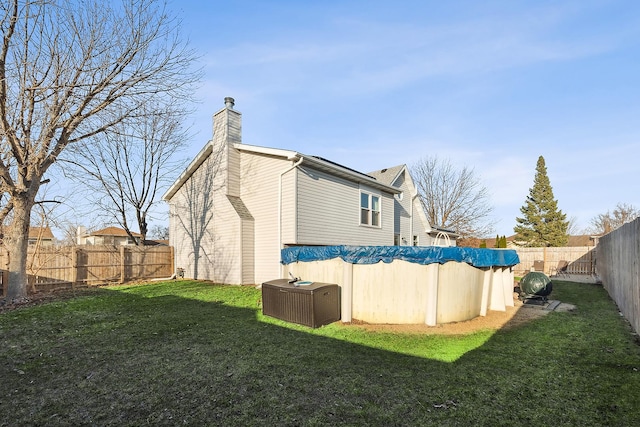 rear view of property featuring a yard, central AC, a fenced backyard, and a chimney