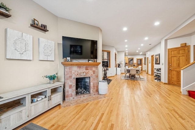 living area featuring recessed lighting, light wood-type flooring, stairs, and a tiled fireplace