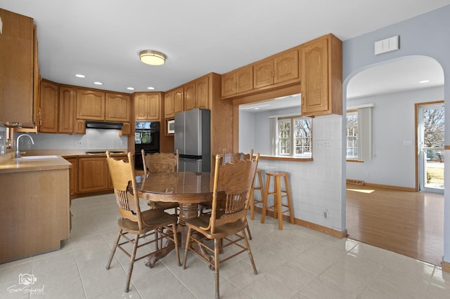 kitchen with light tile patterned flooring, arched walkways, a sink, under cabinet range hood, and appliances with stainless steel finishes