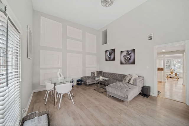 living area featuring visible vents, baseboards, a towering ceiling, and light wood finished floors