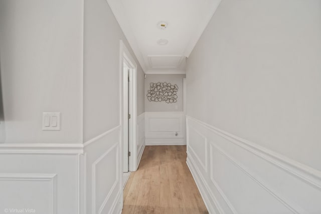 hall featuring a decorative wall, attic access, wainscoting, and light wood finished floors