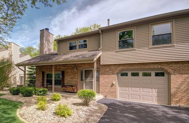 view of front facade with an attached garage, brick siding, covered porch, and a chimney