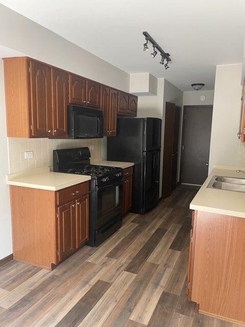 kitchen with tasteful backsplash, dark wood finished floors, light countertops, black appliances, and a sink