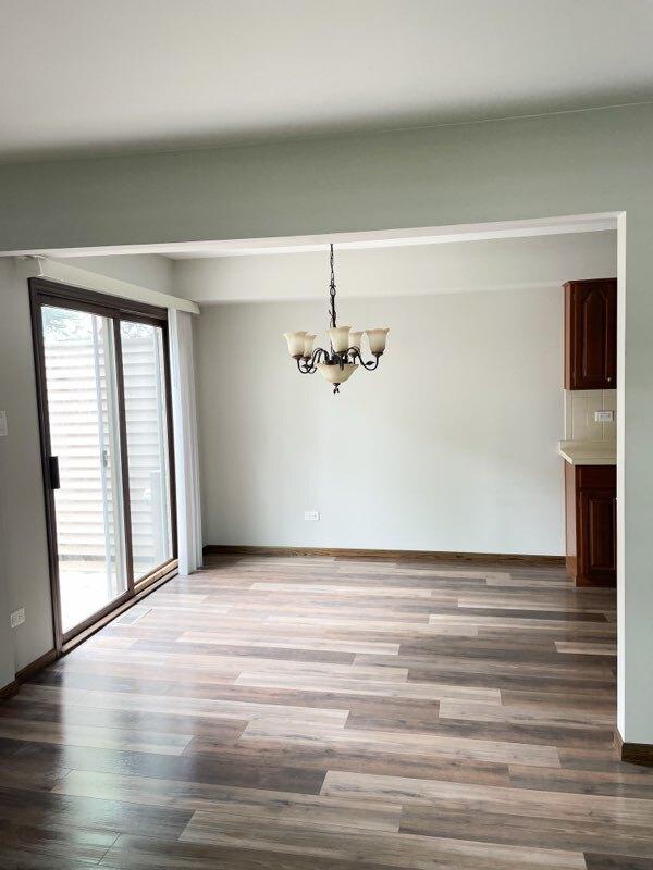 unfurnished dining area featuring an inviting chandelier, wood finished floors, and baseboards