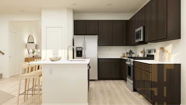 kitchen featuring light wood finished floors, dark brown cabinets, light countertops, appliances with stainless steel finishes, and a kitchen island with sink