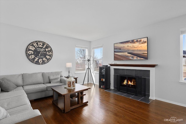 living room featuring a tile fireplace, baseboards, and wood finished floors