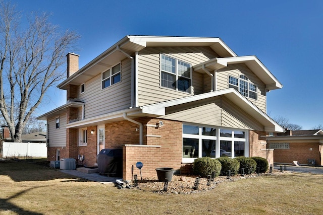 rear view of property featuring brick siding, central AC unit, a lawn, and a chimney