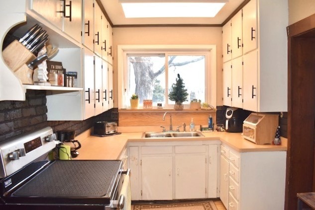 kitchen featuring a sink, light countertops, decorative backsplash, stainless steel range with electric stovetop, and open shelves