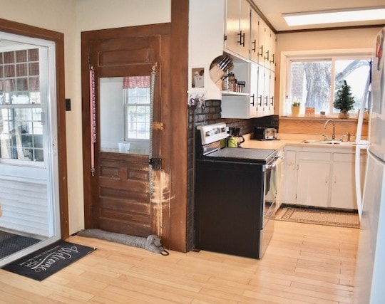 kitchen with stainless steel range with electric stovetop, a sink, light wood-style floors, white cabinets, and light countertops