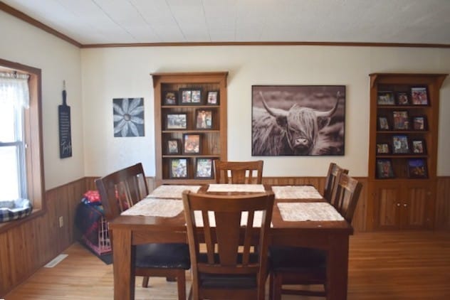 dining space featuring ornamental molding, light wood-style flooring, wainscoting, and wood walls