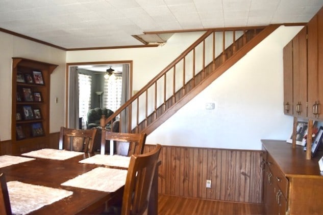 dining room featuring wooden walls, ceiling fan, stairs, wainscoting, and wood finished floors