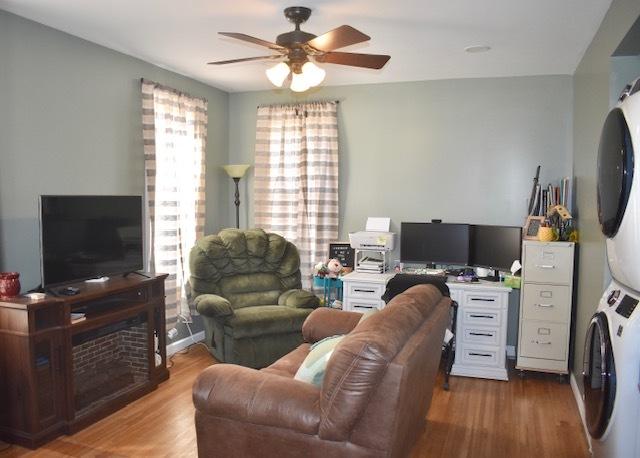 living room featuring wood finished floors, stacked washer / dryer, and a ceiling fan