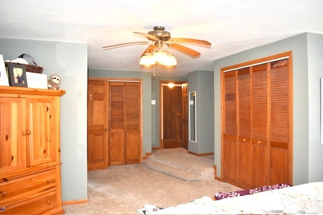 bedroom featuring ceiling fan, light colored carpet, multiple closets, and baseboards