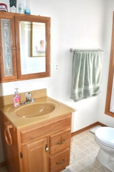 half bathroom with toilet, vanity, and baseboards