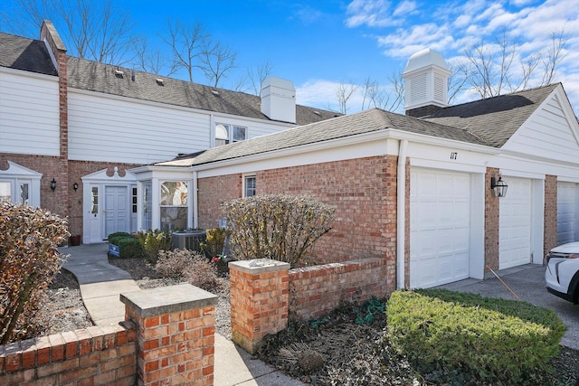 view of home's exterior with brick siding, a chimney, a garage, and a shingled roof