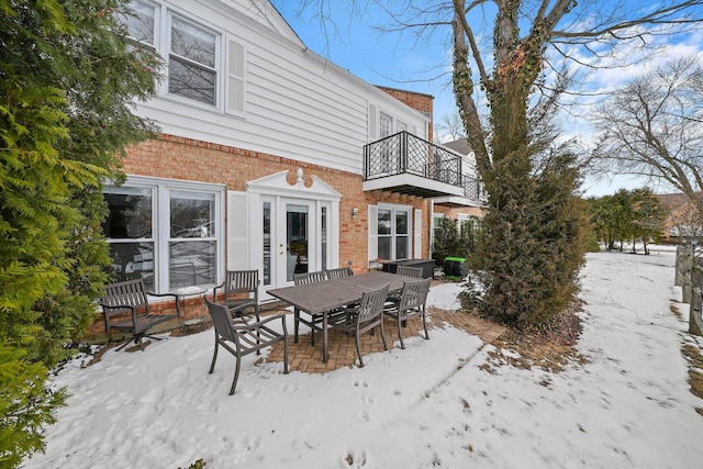 snow covered house featuring brick siding, outdoor dining area, and a balcony